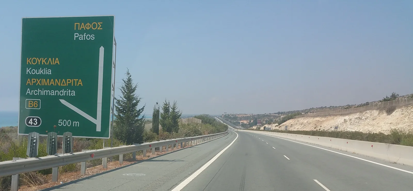 A green motorway sign for Paphos and Kouklia beside a dual carriageway in Cyprus